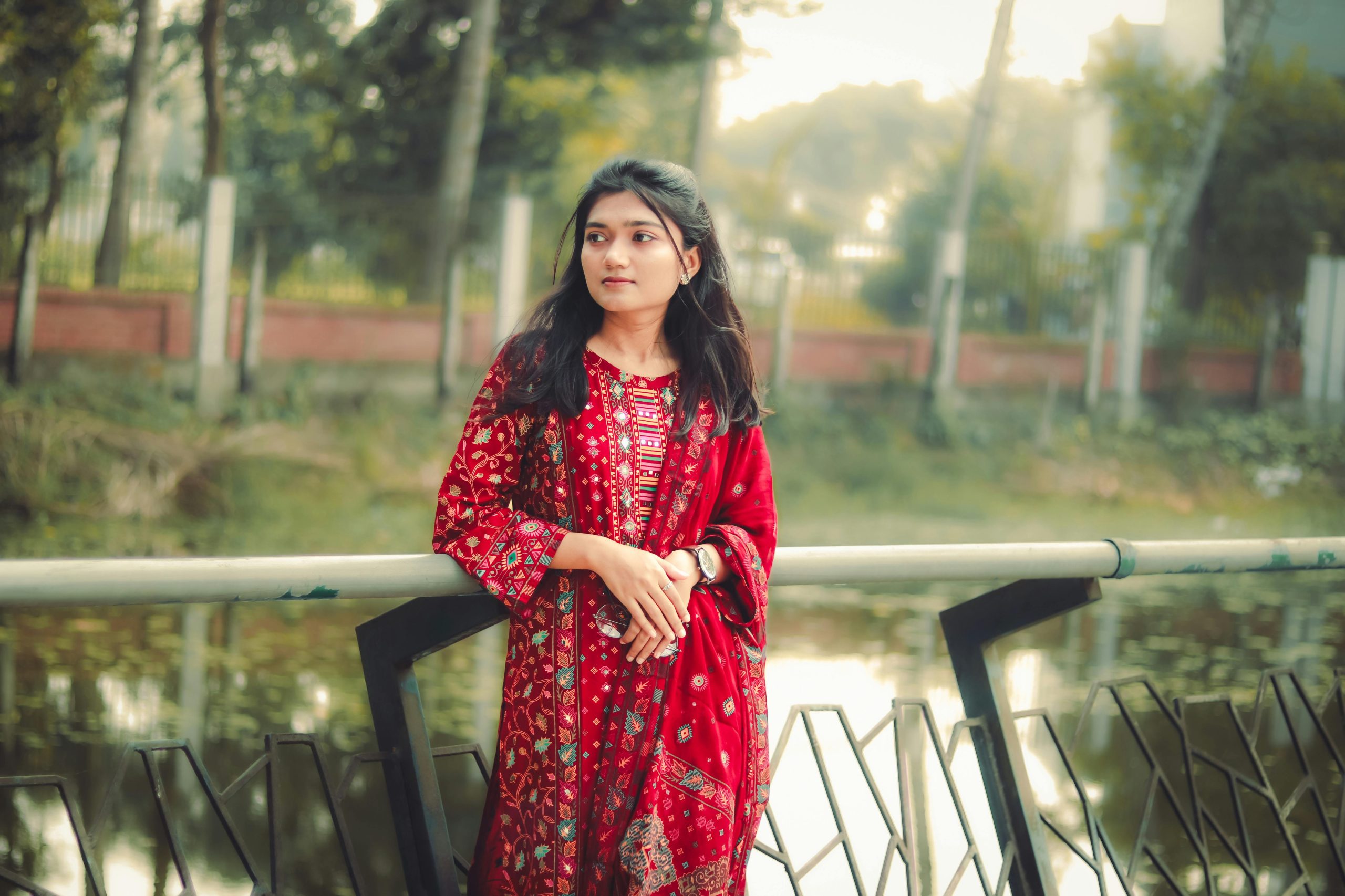 A young woman in vibrant traditional attire stands by a serene lake in Khulna, Bangladesh.